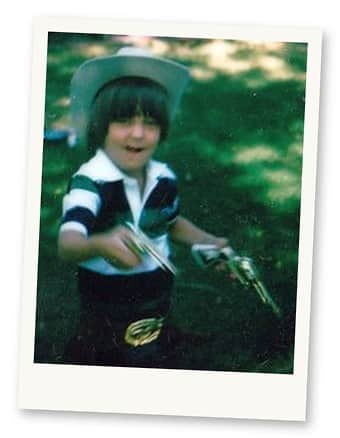 Michael Romano as a young child in a cowboy hat holding two cap guns