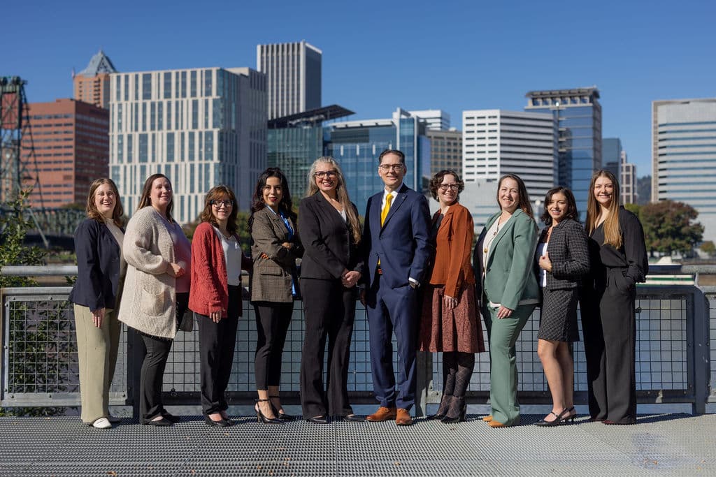 Romano Law, P.C. attorneys and staff standing together beside the Willamette River with the downtown Portland, Oregon, skyline behind them.